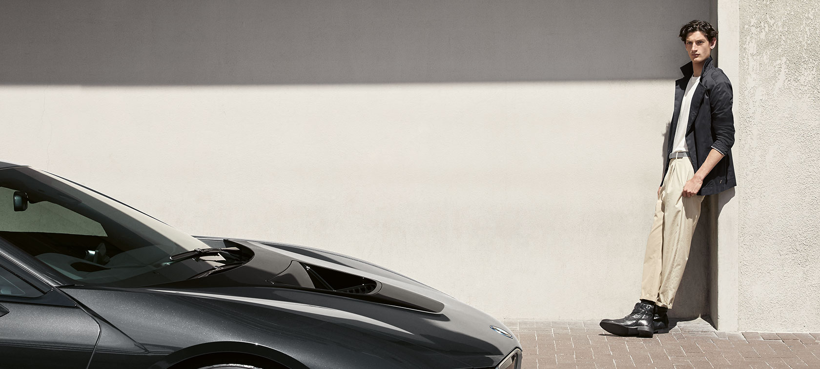 A young man leaning against a wall casually presents products from the BMW i Collection.